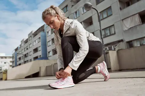 Läuferin kniet am Boden und bindet ihre neuen, pinken Laufschuhe ein. Perfekt zum Einlaufen!