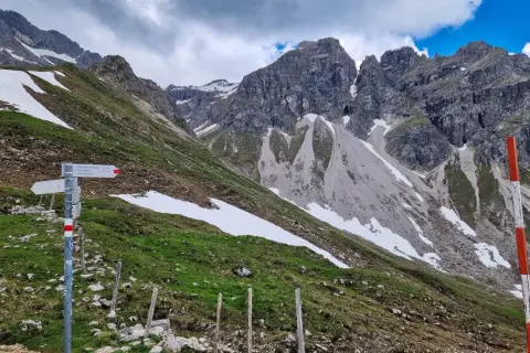 Wanderwegweiser am Widderstein Trail. Grüne Hänge mit Schneefeldern und steile Felsgipfel im Hintergrund.