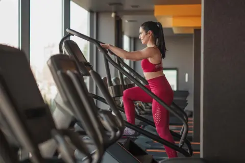 Frau im Fitnessstudio macht ein Stairmaster Workout. Sie trägt ein rotes Sport-Outfit und trainiert intensiv.