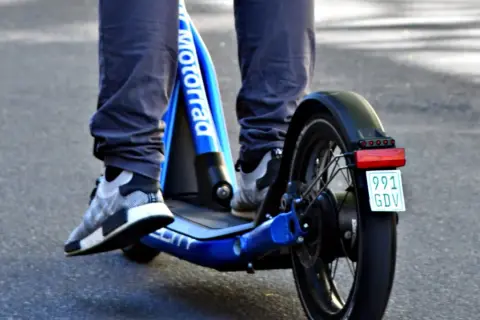 Ein e scooter fahrer auf einem blauen Roller mit dem Schriftzug "Motorrad" und einem Kennzeichen.