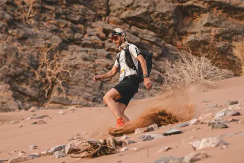 Läufer im Marathon des Sables wirbelt Sand auf. Die extreme Wüstenlandschaft fordert alles.