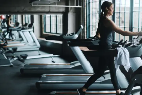 Frau im Fitnessstudio beim Laufband Training, mit Kopfhörern und Wasserflasche.