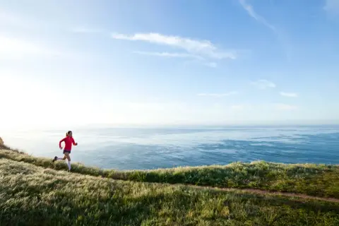 Läuferin auf Küstenpfad, trainiert für Marathon unter 4 Stunden. Weite See und Himmel.