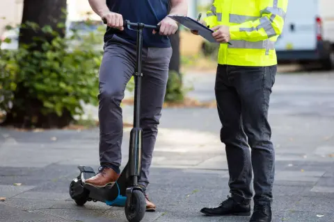 Mann auf e-scooter in Spanien, während ein anderer Mann mit Warnweste Notizen macht.