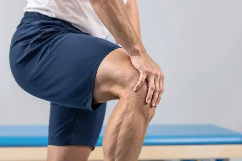 Mann hält schmerzgebeugt sein Knie, nachdem es laut knackte.