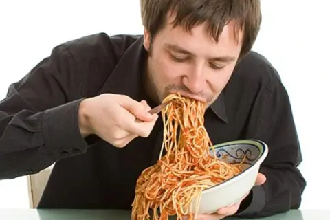 Mann isst genüsslich eine riesige Portion Spaghetti mit Tomatensoße. Perfekt für das Carb Loading vor dem Wettkampf!