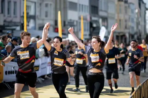 Läufer feiern Zieleinlauf beim Marathon. Ein Mann und zwei Frauen mit Startnummern, die Teil des Marathon Kalenders sind, jubeln.