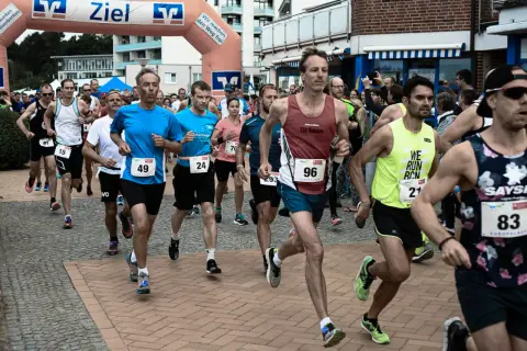 Läufer beim Europalauf Neustadt, einige mit Startnummern wie 49, 96 und 21. Sie rennen unter einem Zielbogen hindurch.