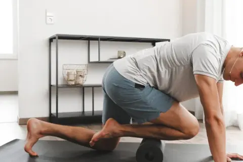 Mann massiert mit Foam Roller seinen vorderen Schienbeinmuskel, um Schmerzen zu lindern.