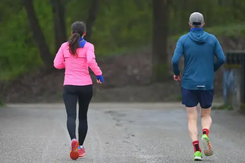 Zwei Läufer, eine Frau in Pink und ein Mann in Blau, genießen die frische Luft. Sie zeigen, was bringt joggen: Fitness und Wohlbefinden.