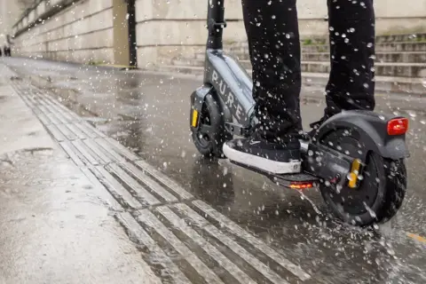 Ein e-scooter bei regen spritzt durch Pfützen auf dem nassen Gehweg.
