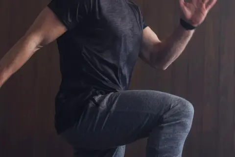 Mann in Sportkleidung, der auf der Stelle läuft, mit erhobenem Knie und ausgestrecktem Arm.