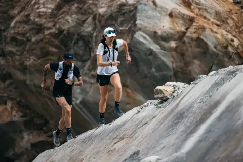 Zwei Läufer meistern einen steilen, felsigen Hang. Sie sind Teil eines Ultramarathons, einer extremen Laufdisziplin.