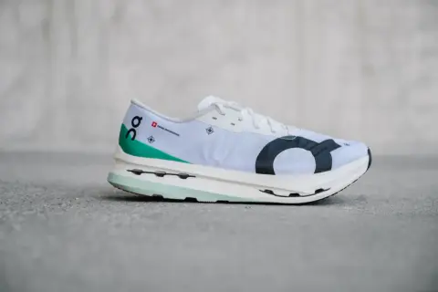 Weißer Laufschuh, On Cloudboom Echo 3, mit grünen Akzenten und schwarzem Logo.