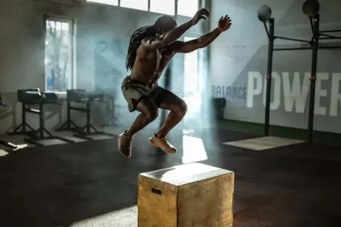 Mann macht explosive Box Jumps in einem Fitnessstudio. Rauch und Lichteffekte unterstreichen die Dynamik.
