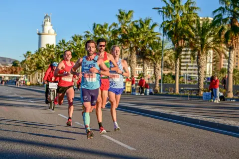 Läufer beim Malaga Marathon, vorbei an Palmen und dem Leuchtturm.