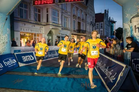 Läufer im Ziel beim hella marathon rostock. Gelbe Trikots mit "Ambulanz Millich" und Startnummern.