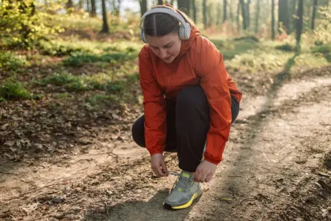 Frau mit Kopfhörern bindet ihre Laufschuhe auf einem Waldweg. Joggen im Alter ist eine tolle Möglichkeit, fit zu bleiben.