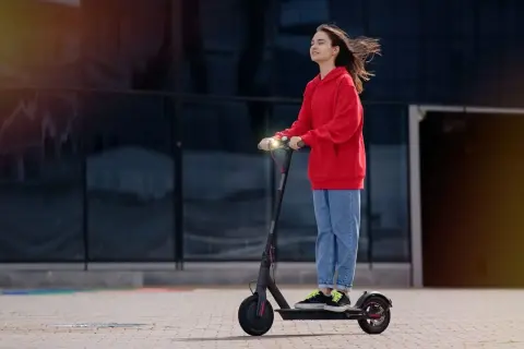 Junge Frau auf E-Scooter, genießt die Fahrt. Ab wann darf man E-Roller fahren? Ab 14 Jahren mit Zustimmung der Eltern.