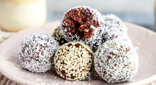Leckeres energy balls rezept: Schokoladige Kugeln mit Kokosraspeln und Sesam auf einem Teller.