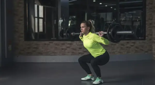 Frau macht Kniebeugen mit Langhantel. Sie ist fokussiert und stark, bereit für ihr Training. Kiffen und Sport – eine Kombination, die sie inspiriert.