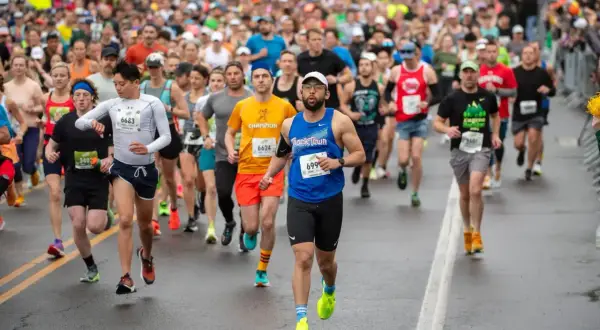 Läufer beim Halbmarathon Europa. Viele Teilnehmer in bunten Trikots, einige mit Startnummern, kämpfen sich über die nasse Straße.