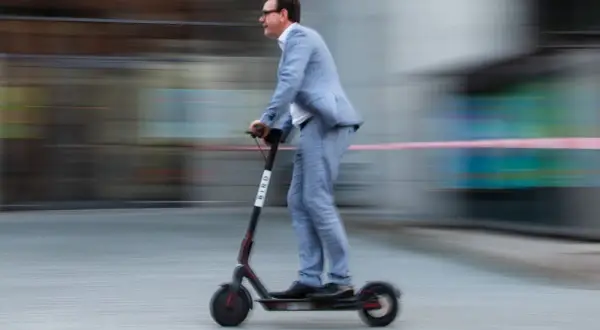 Mann im Anzug fährt mit einem E-Scooter durch Belgien.