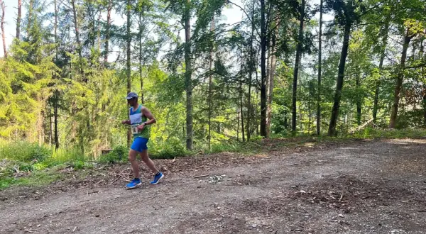 Läufer mit Startnummer 18 beim Plankenfelser Waldlauf, umgeben von hohen Bäumen und Sonnenschein.