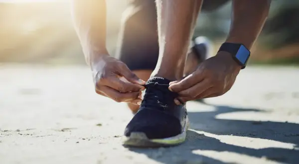 Hände binden die Schnürsenkel von Laufschuhen. Die Sonne scheint warm auf den Sand.