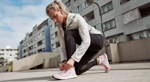 Läuferin kniet am Boden und bindet ihre neuen, pinken Laufschuhe ein. Perfekt zum Einlaufen!