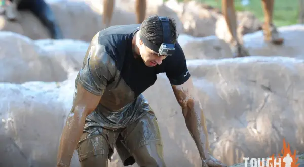 Ein Mann kämpft sich durch den Schlamm bei einem Tough Mudder **obstacle run**. Er trägt eine GoPro am Kopf.