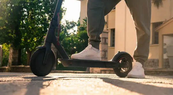 Person steht auf einem e scooter ohne kennzeichen, bereit für die Fahrt im warmen Sonnenlicht.