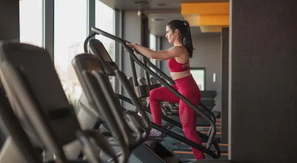 Frau im Fitnessstudio macht ein Stairmaster Workout. Sie trägt ein rotes Sport-Outfit und trainiert intensiv.