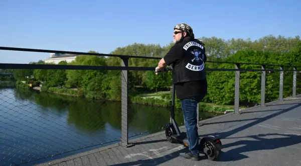 Mann auf E-Scooter mit "TRITTBRETT GERMANY" Aufnäher auf Weste. Er erklärt, wie funktioniert ein E-Scooter, während er auf einer Brücke steht.