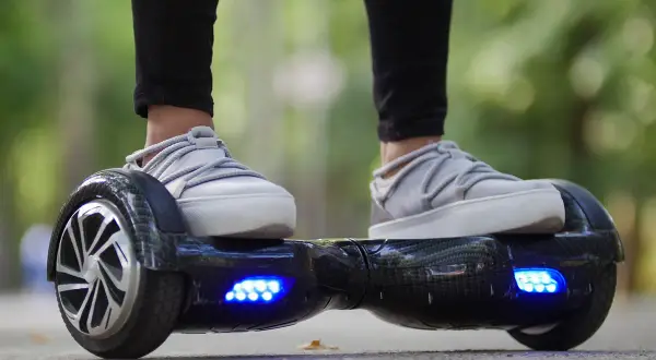 Person fährt Hoverboard mit leuchtenden blauen Lichtern. Die Frage "wie lange braucht ein Hoverboard zum laden?" beschäftigt viele Nutzer.