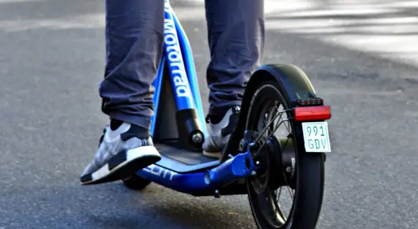 Ein e scooter fahrer auf einem blauen Roller mit dem Schriftzug "Motorrad" und einem Kennzeichen.
