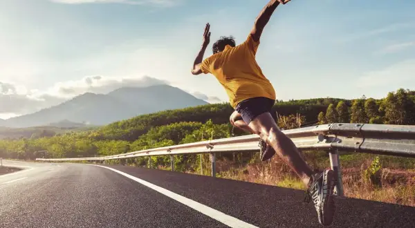Läufer auf einer Straße, der sich fragt, wie wird man schneller. Bergige Landschaft im Hintergrund.