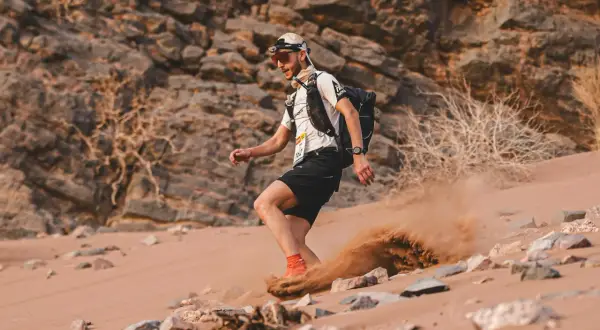 Läufer im Marathon des Sables wirbelt Sand auf. Die extreme Wüstenlandschaft fordert alles.