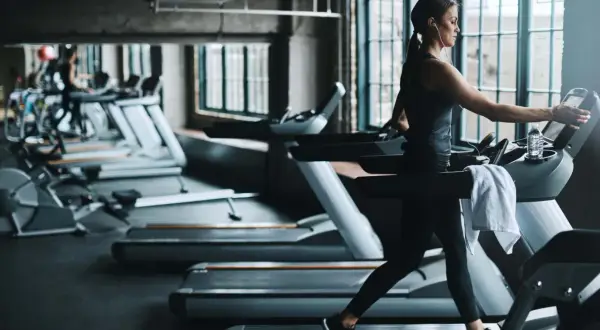 Frau im Fitnessstudio beim Laufband Training, mit Kopfhörern und Wasserflasche.