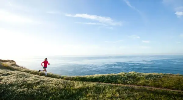 Läuferin auf Küstenpfad, trainiert für Marathon unter 4 Stunden. Weite See und Himmel.