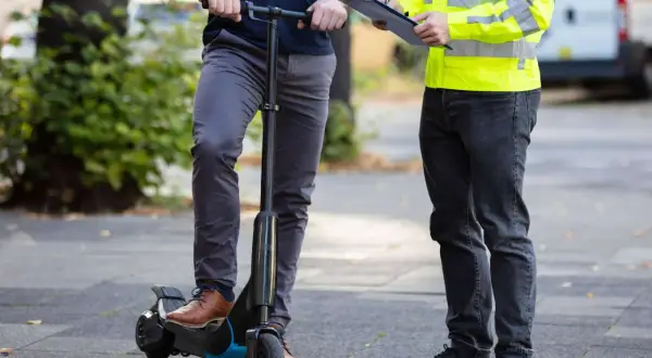 Mann auf e-scooter in Spanien, während ein anderer Mann mit Warnweste Notizen macht.