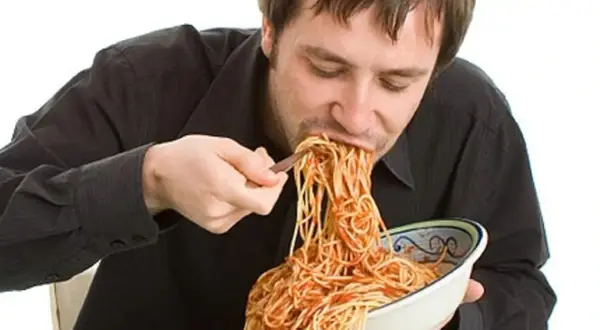 Mann isst genüsslich eine riesige Portion Spaghetti mit Tomatensoße. Perfekt für das Carb Loading vor dem Wettkampf!
