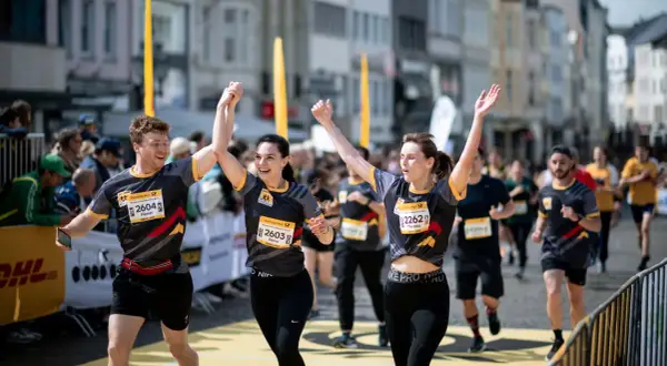 Läufer feiern Zieleinlauf beim Marathon. Ein Mann und zwei Frauen mit Startnummern, die Teil des Marathon Kalenders sind, jubeln.