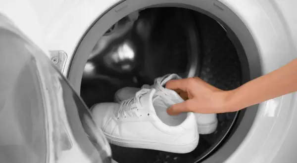 Weiße Laufschuhe werden in eine Waschmaschine gelegt.