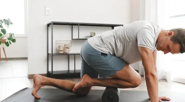 Mann massiert mit Foam Roller seinen vorderen Schienbeinmuskel, um Schmerzen zu lindern.
