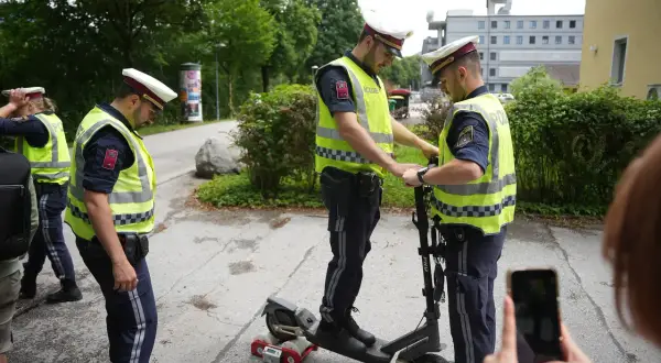 Polizisten prüfen einen E-Scooter. Einer steht drauf, der andere hält ihn fest. Ein Messgerät ist am Hinterrad angebracht.