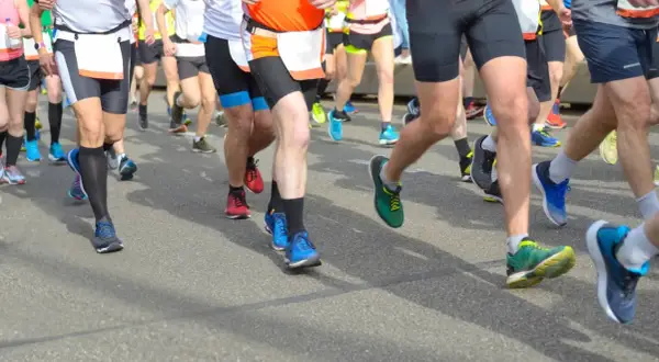 Läufer im Halbmarathon kämpfen um die beste Zeit. Bunte Laufschuhe und kurze Hosen dominieren das Bild.