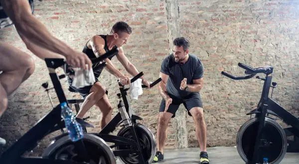 Männer trainieren intensiv beim Spinning. Ein Trainer motiviert die Sportler, die auf ihren Rädern strampeln.
