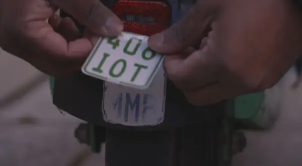 Hände befestigen ein neues e-scooter nummernschild mit der Aufschrift "408 10T" über einem alten, abgenutzten Kennzeichen.
