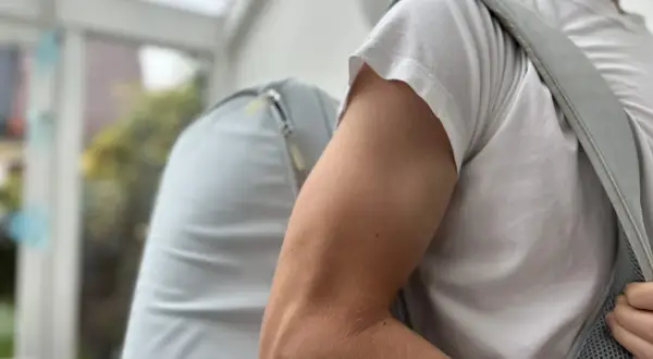 Mann mit Rucksack, der beim Anziehen der Jacke **Schmerzen im Oberarm** spürt.